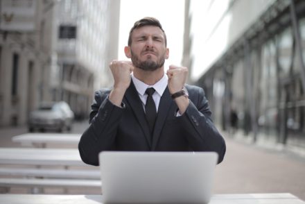 man in black suit sitting on chair beside buildings